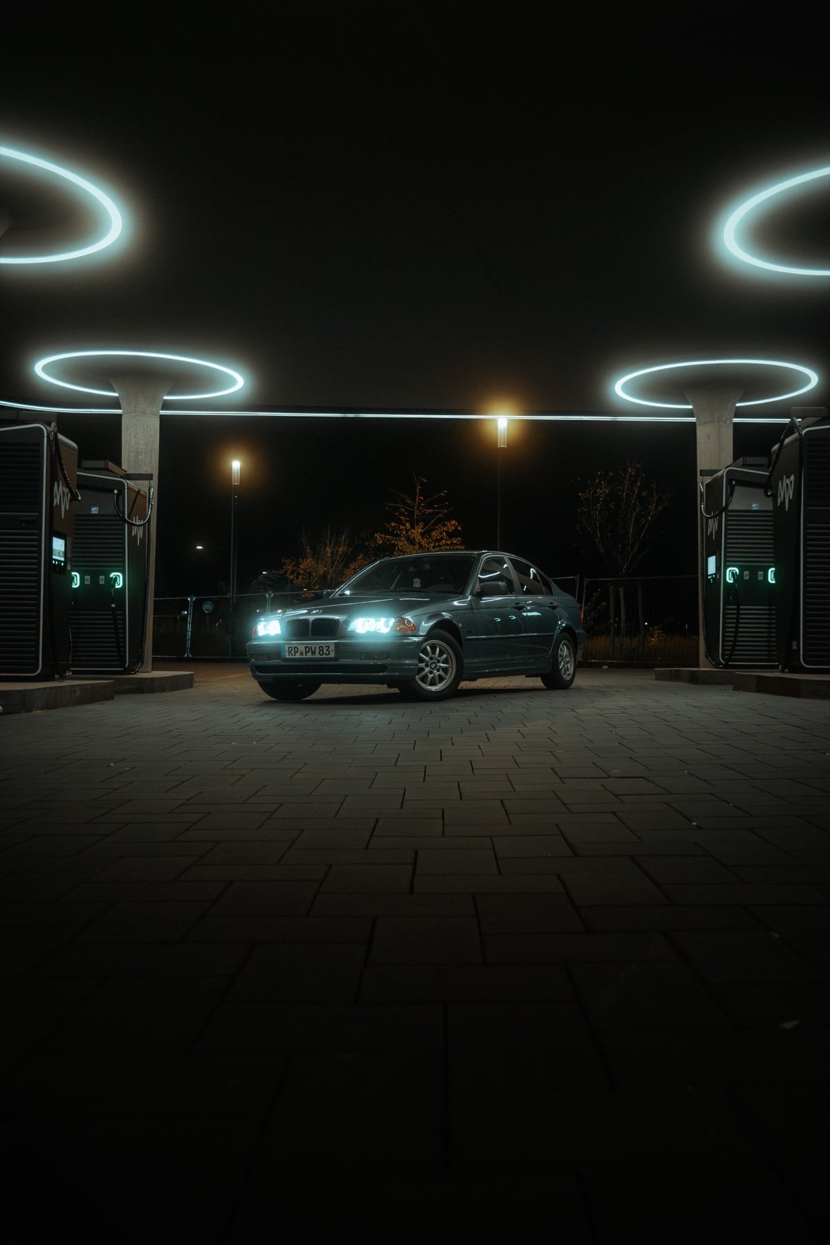 Grüner BMW 3er zwischen zwei beleuchteten Ladesäulen mit kreisrunden Neonringen