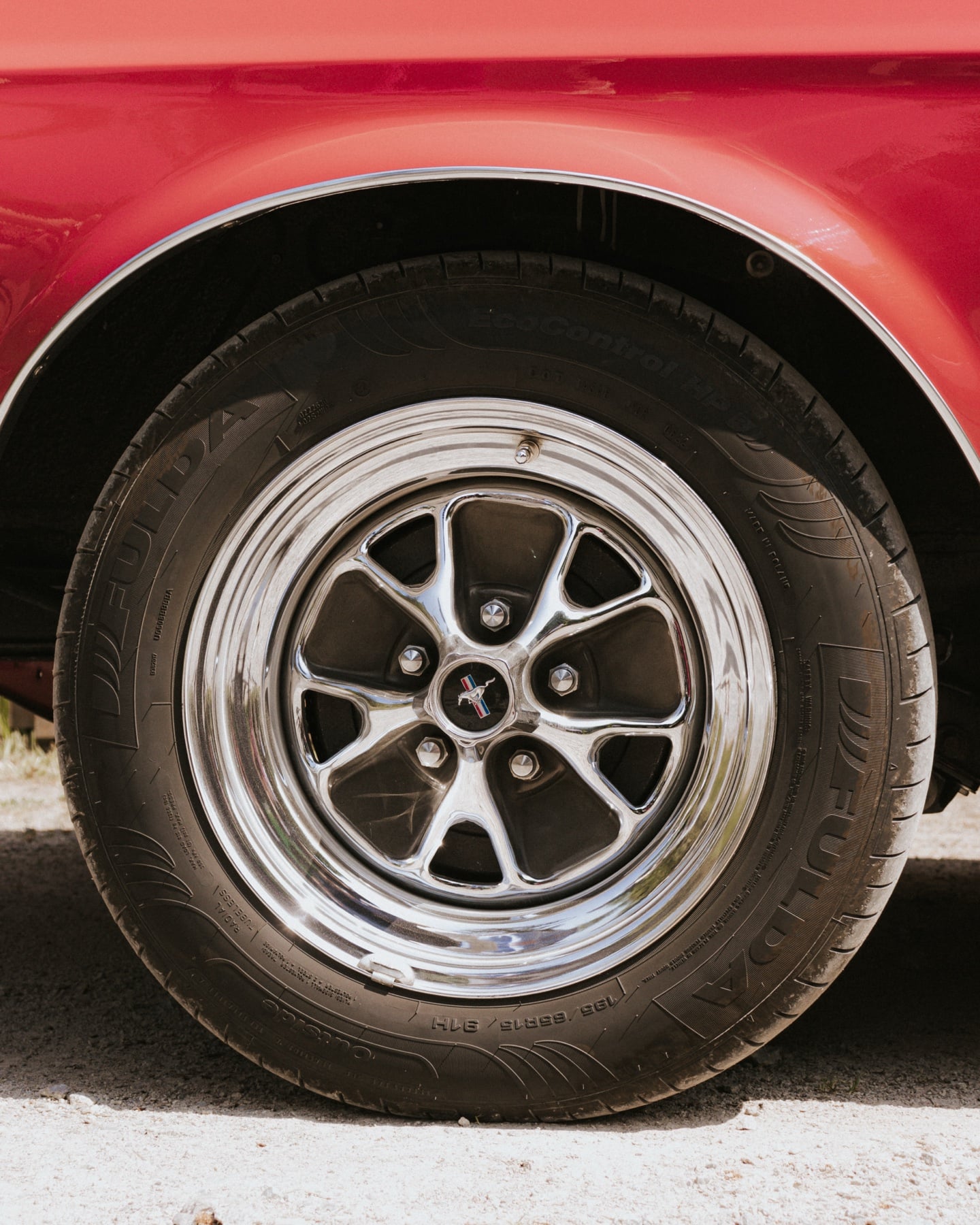 Verchromte Felge eines roten Ford Mustang mit Pony-Emblem in der Nabenkappe