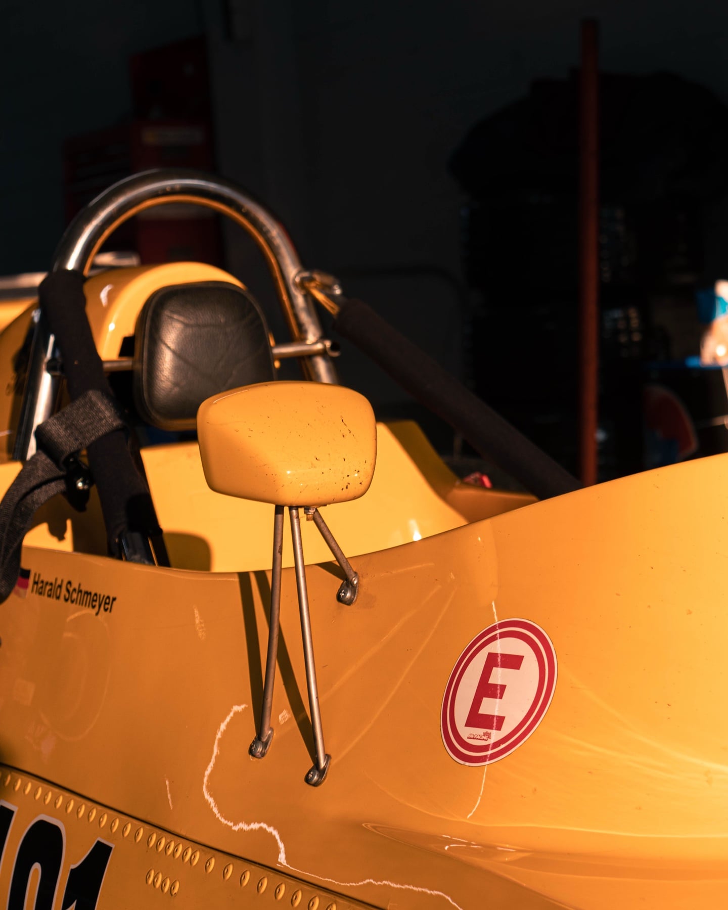 Detail des Fahrersitzes eines gelben historischen Formel-Wagens mit Sicherheitsgurten und E-Sticker