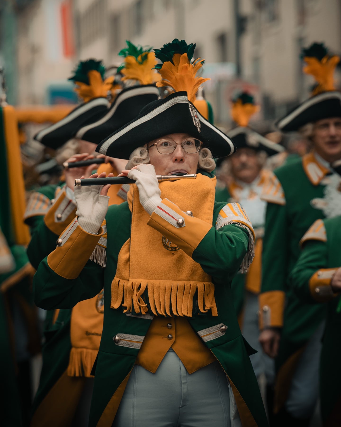 Karnevalsmusikerin in grün-gelber Funkenuniform mit Dreispitz und Federn beim Spiel der Querflöte