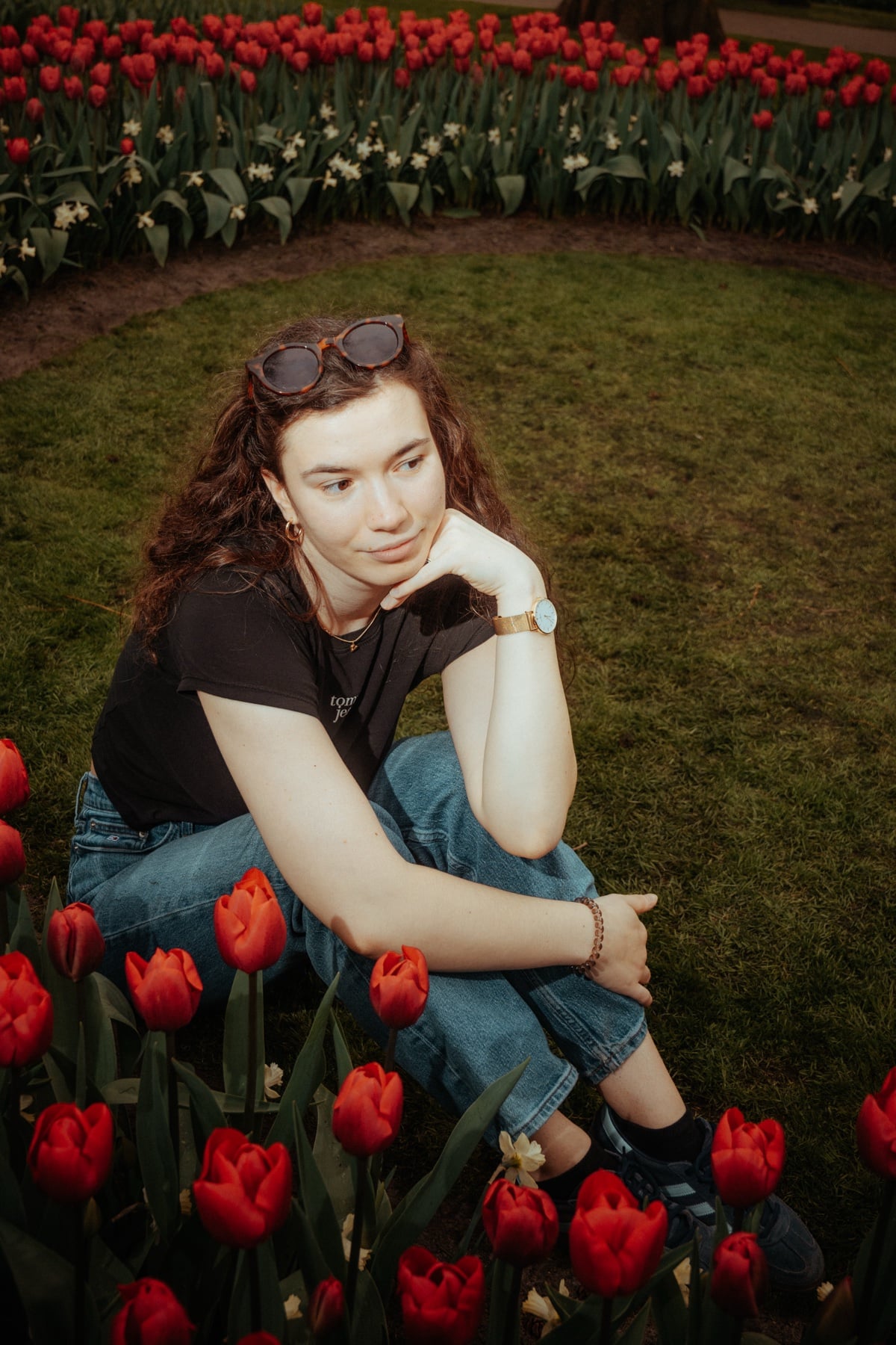 Junge Frau sitzt nachdenklich zwischen roten Tulpen am Rand eines Beetes