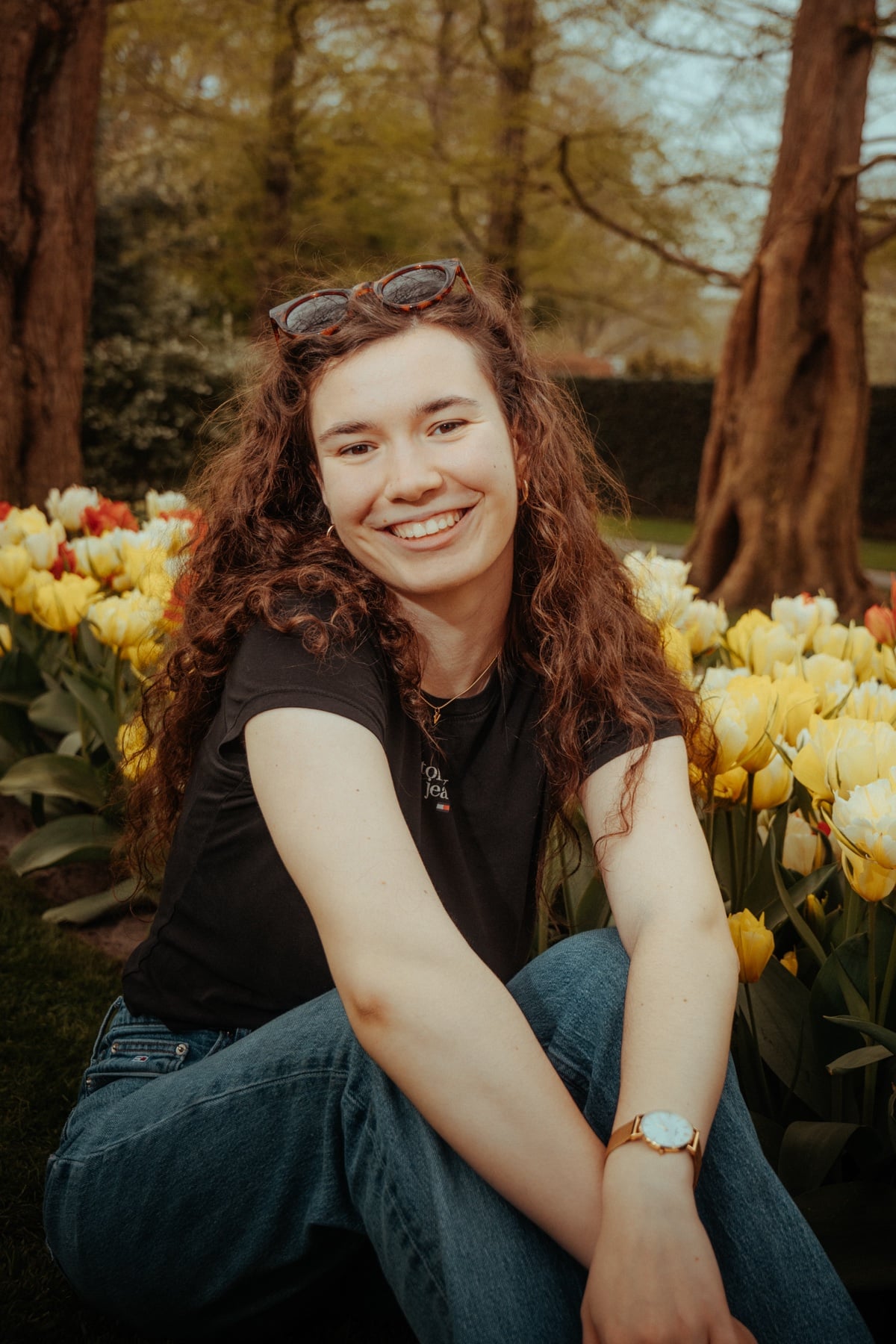 Lachende Frau mit Locken und Sonnenbrille im Haar zwischen gelben Tulpen