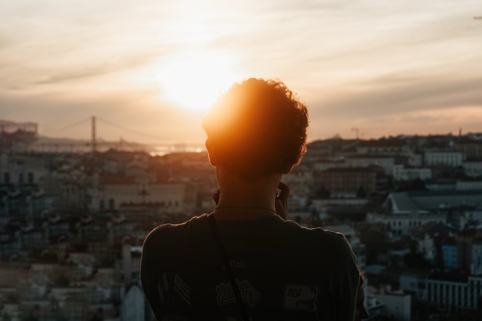 Silhouette eines Mannes mit Locken vor der Skyline Lissabons im goldenen Abendlicht