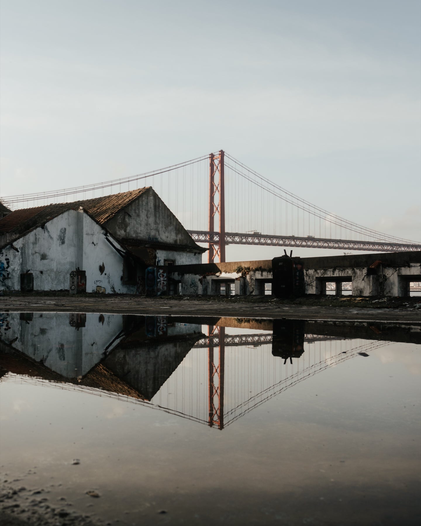 Verlassenes Hafengebäude in Lissabon mit Spiegelung der Ponte 25 de Abril in einer Pfütze