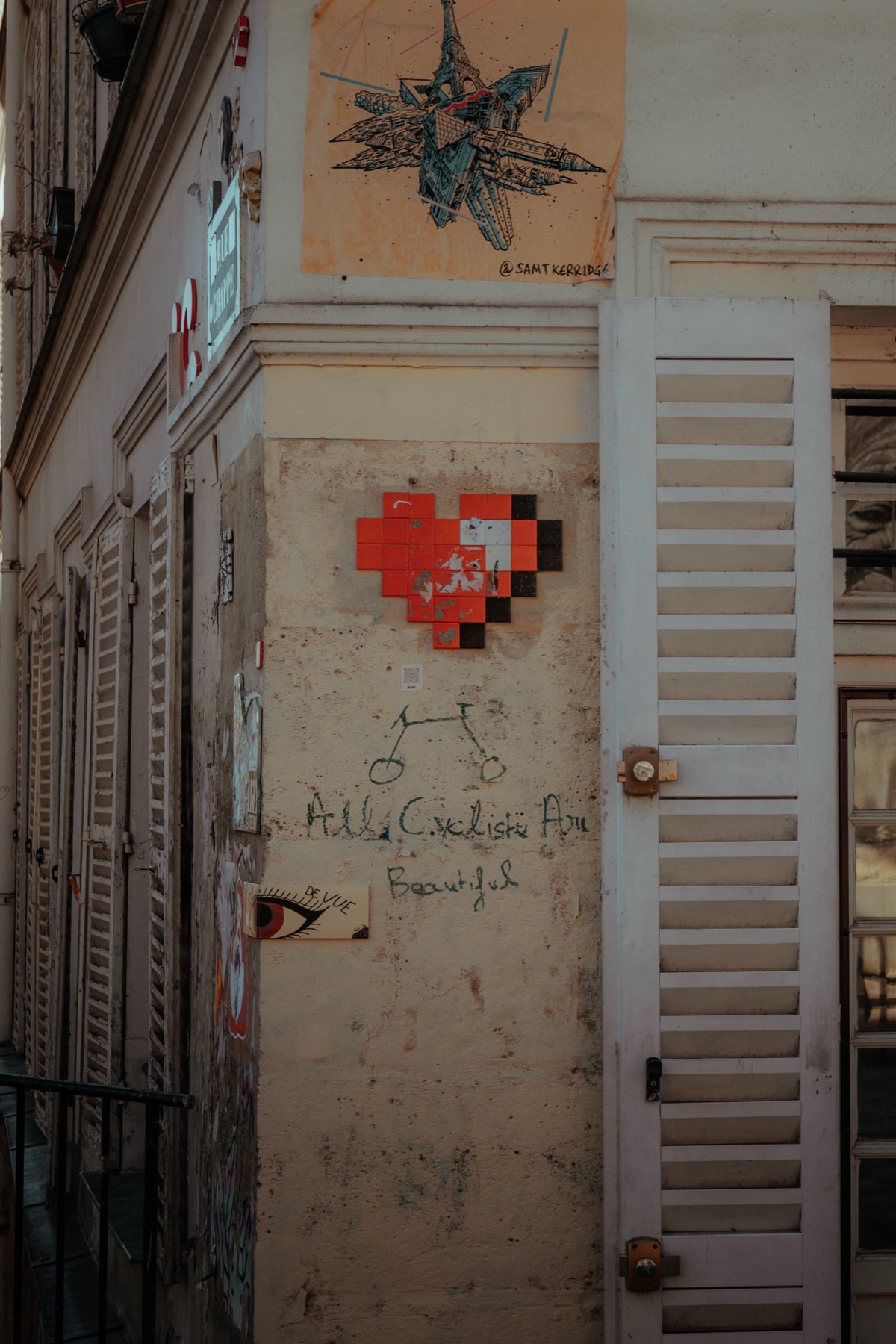 Pixelherz-Mosaik von Space Invader an einer Pariser Hauswand neben einem Graffiti-Auge