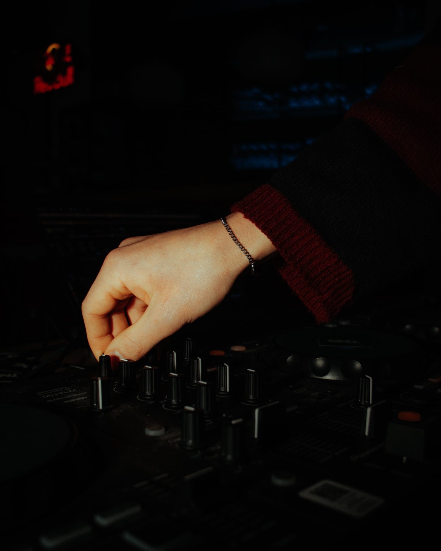 Hand am DJ-Mixer mit silbernem Armband, dunkler Booth-Hintergrund mit roter LED-Anzeige