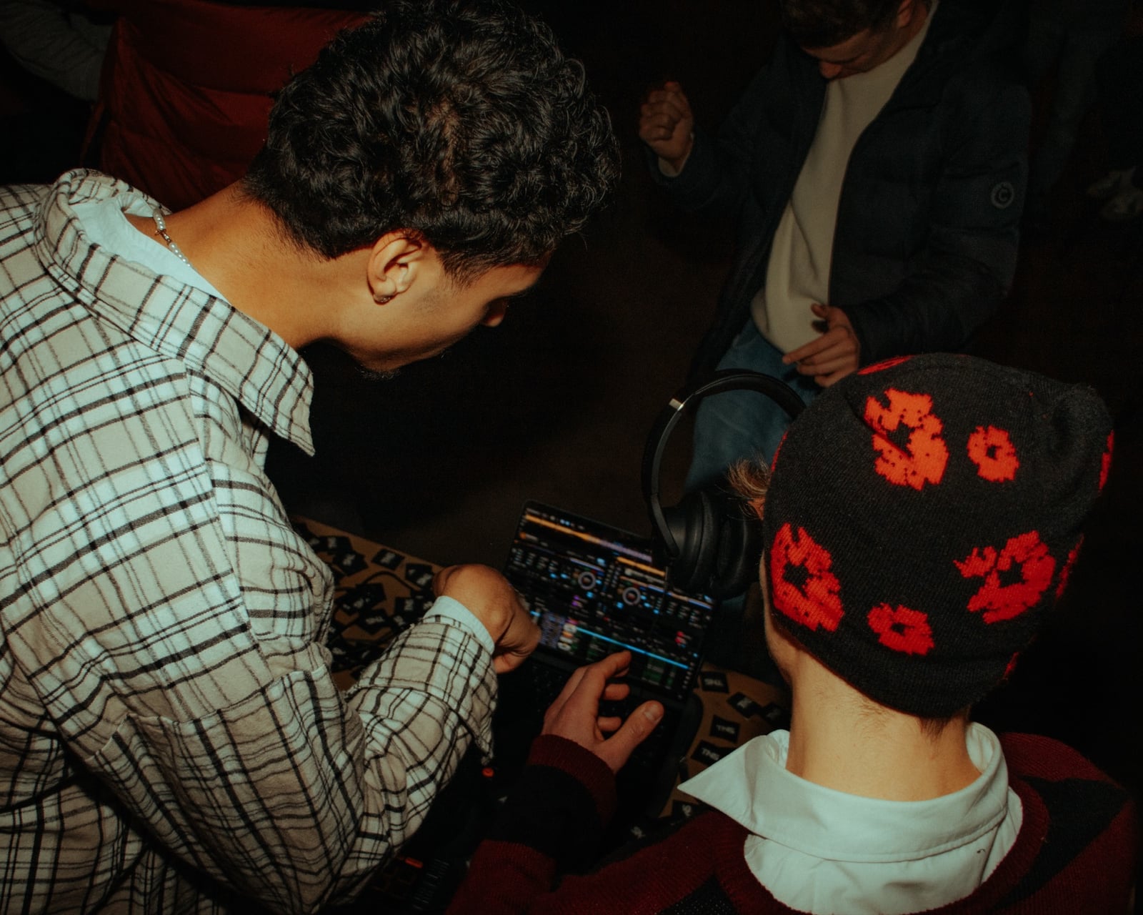 Zwei DJs in der Booth schauen aufs Display des Pioneer-Decks, eine Person trägt eine rot-schwarze Mütze