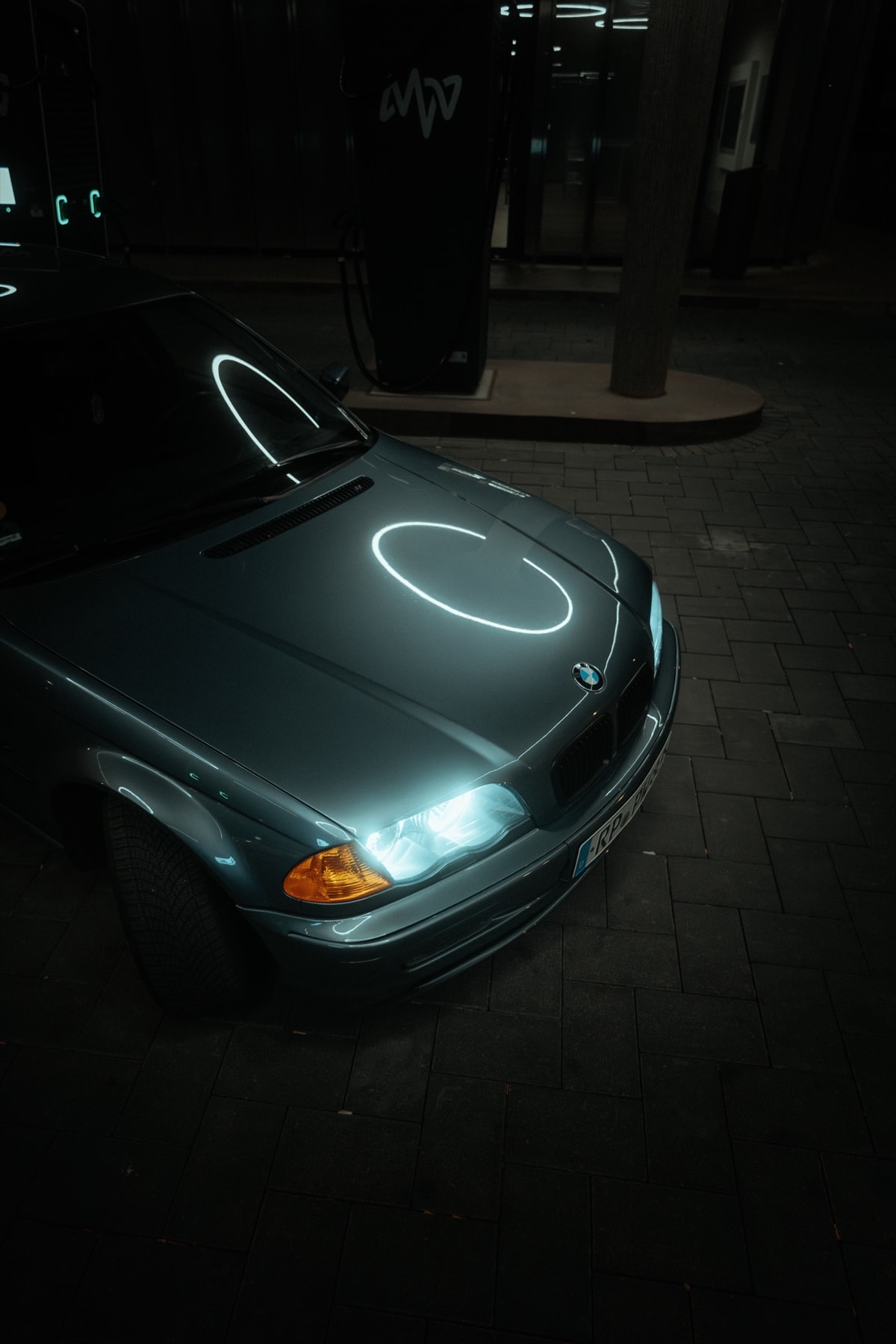Grüner BMW 3er bei Nacht an einer Schnellladesäule, Lichtreflex auf der Motorhaube
