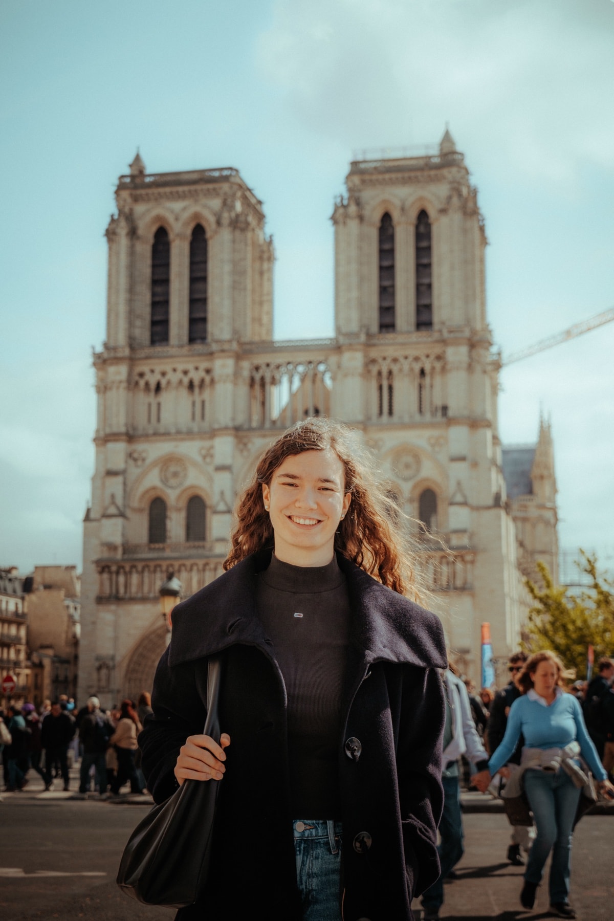 Lachende Frau mit Locken im dunklen Wollmantel vor Notre-Dame